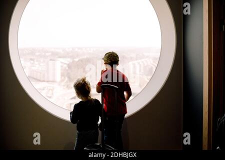 Les frères et sœurs regardent par la fenêtre tout en étant debout dans la chambre d'hôtel Banque D'Images