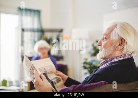 Homme senior lisant le journal tout en étant assis sur un canapé dans un centre de soins infirmiers accueil Banque D'Images