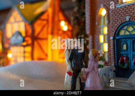 Une scène de vacances miniature de village de Noël avec une mariée et un marié embrassant devant une église comme une jeune fille de fleurs montres. Banque D'Images