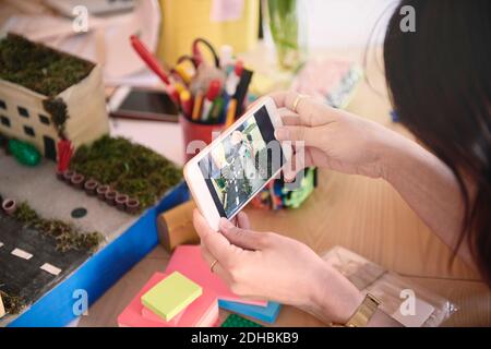 Image rognée d'une femme ingénieure photographiant un modèle architectural sur mobile téléphone à la table dans le bureau Banque D'Images