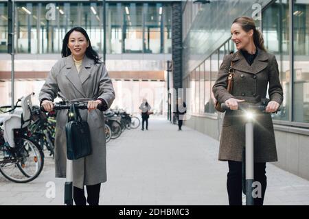 Des femmes souriantes qui voyagent en scooter électrique sur la piste de marche bâtiment en ville Banque D'Images