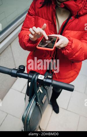 Section basse de l'appareil de commutation femelle scannant le code QR sur électrique poussez le guidon du scooter avec le smartphone Banque D'Images