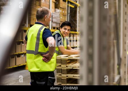Jeune travailleur souriant regardant un collègue senior se tenant à la distribution entrepôt Banque D'Images