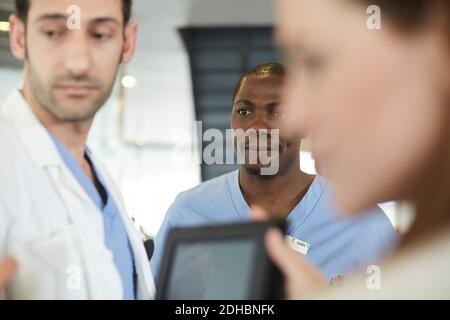 Les professionnels de la santé multiethniques discutent sur tablette numérique dans le hall d'entrée à hôpital Banque D'Images