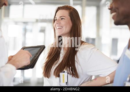 Des professionnels de santé multiethniques souriants discutent sur une tablette numérique dans le hall à l'hôpital Banque D'Images