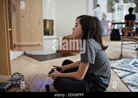 Vue latérale d'un garçon qui regarde loin pendant qu'il joue à un jeu vidéo sur parquet à la maison Banque D'Images