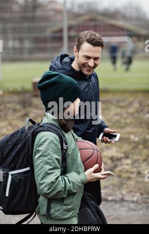 Un père et un fils souriants parlent tout en marchant dans la rue après pratique du basket-ball en hiver Banque D'Images