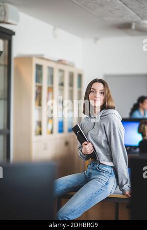 Portrait d'une étudiante confiante assise avec des livres sur le bureau en classe à l'école secondaire Banque D'Images