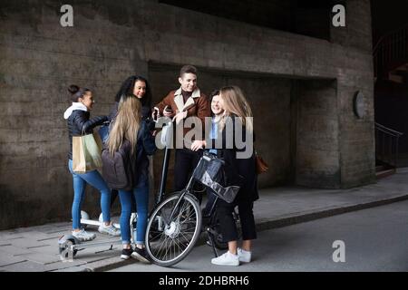 Des amis hommes et femmes souriants avec des scooters de poussée et vélo sur sentier Banque D'Images