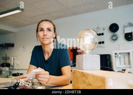 Une femme attentionnés qui regarde à l'extérieur tout en étant assise à l'établi bureau créatif Banque D'Images