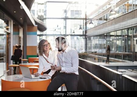 Des collègues souriants discutent sur un ordinateur portable dans l'atrium Banque D'Images