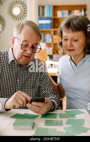 Travailleur social féminin mature aidant l'homme âgé retraité à utiliser smartphone à la table dans la maison de soins Banque D'Images