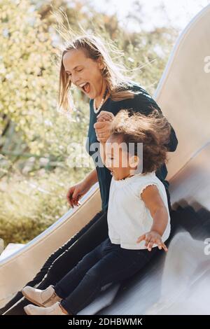 Bonne mère glissant avec fille sur le toboggan au parc Banque D'Images