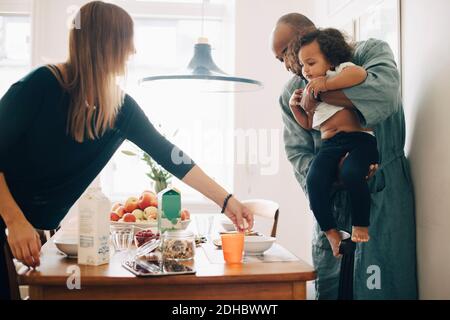 Père faisant la fille s'asseoir sur une chaise tandis que la mère sert le petit-déjeuner à la table Banque D'Images