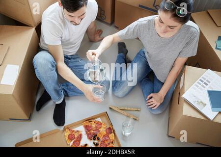 Femme servant de l'eau à l'homme tout en ayant de la pizza pendant le déplacement de nouvelle maison Banque D'Images