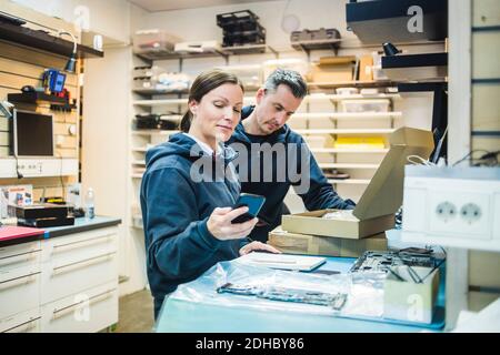 Femme ingénieur mature utilisant un téléphone portable par un collègue dans l'atelier Banque D'Images