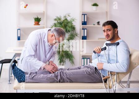 Jeune jambe blessée homme en visite avec un vieux médecin ostéopathe Banque D'Images