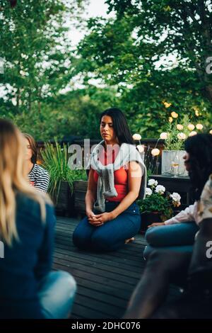 Femme adulte de taille moyenne assise avec les yeux fermés par des amis balcon pendant la session de groupe Banque D'Images