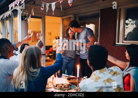 Homme et femme embrassant pendant le dîner avec des amis Banque D'Images
