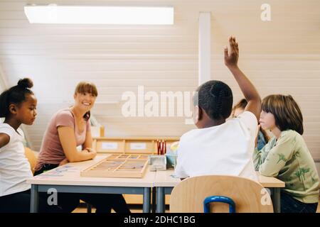 Enseignant regardant un garçon levant la main tout en répondant en classe Banque D'Images