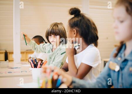 Des amis de l'école dessinant sur du papier au bureau dans la salle de classe Banque D'Images