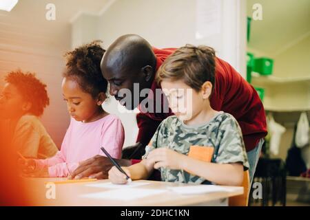 Enseignant de taille moyenne assistant les élèves à leur bureau dans la salle de classe Banque D'Images