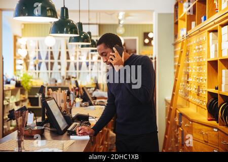 Un jeune homme confiant qui parle sur un smartphone tout en écrivant au comptoir de caisse dans le magasin de meubles Banque D'Images