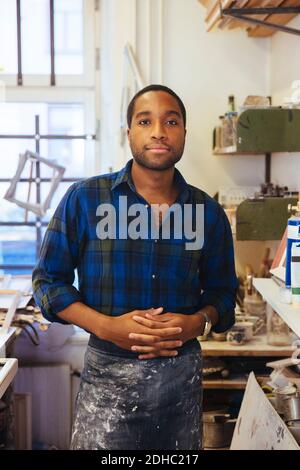 Portrait d'un jeune homme d'artiste de cadrage debout avec les mains jointes à l'atelier Banque D'Images