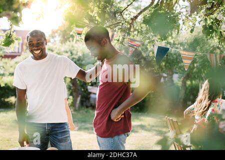 Père souriant qui regarde loin en se tenant près de son fils dans l'arrière-cour pendant la fête Banque D'Images