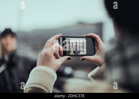 Image rognée d'une femme photographiant un ami avec un smartphone allumé rue en ville Banque D'Images