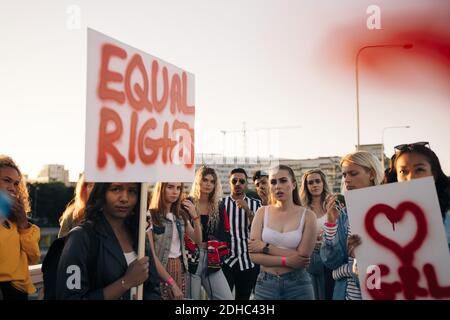 Femmes et hommes avec des affiches de protestation pour l'égalité des droits contre ciel en ville Banque D'Images