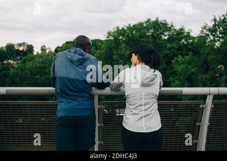 Vue arrière des athlètes masculins et féminins qui parlent tout en se penchant sur la main courante sur la passerelle Banque D'Images