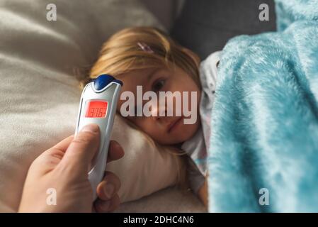 Parent prend de la température pour son enfant avec thermomètre infrarouge à la maison, fièvre de bas grade Banque D'Images