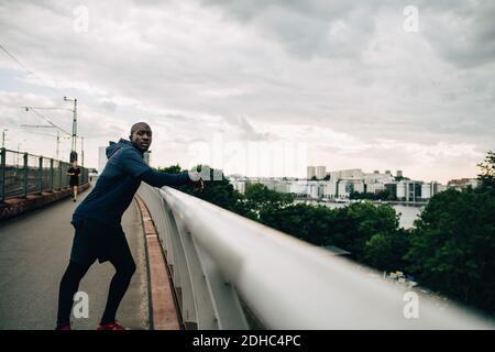 Portrait d'un sportif fatigué penché sur la main courante à la passerelle contre ciel Banque D'Images