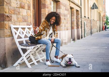 Une femme heureuse assise avec un chien qui prend son selfie sur son téléphone portable au trottoir de la ville Banque D'Images