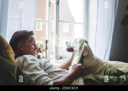 Homme senior lisant le livre tout en se relaxant avec un chien au lit à la maison Banque D'Images