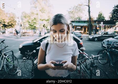 Jeune femme utilisant un téléphone mobile en se tenant sur le trottoir à l'intérieur ville Banque D'Images