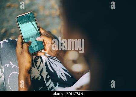 Vue en grand angle d'une jeune femme regardant une photo de plage sur smartphone Banque D'Images