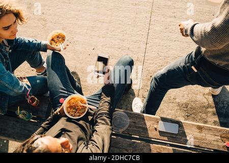 Vue en grand angle de l'adolescent à l'aide d'un smartphone pendant repas avec des amis dans la rue en ville Banque D'Images