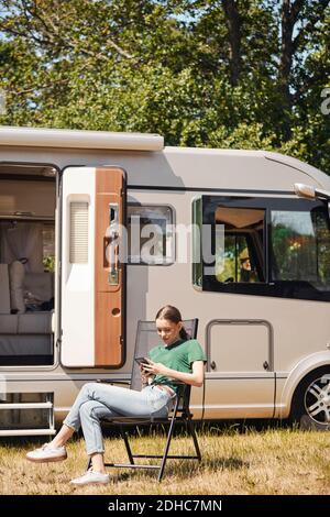 Adolescente utilisant un téléphone portable tout en étant assise sur une chaise pliante en camping-car Banque D'Images