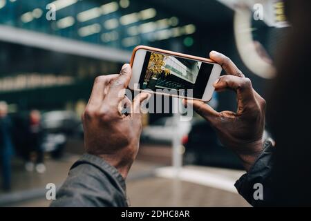 Des mains d'homme d'affaires rognées photographiant le bâtiment avec un smartphone ville Banque D'Images