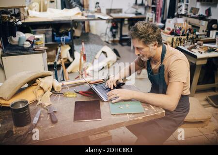 Homme artisan utilisant un ordinateur portable à l'établi dans l'atelier Banque D'Images