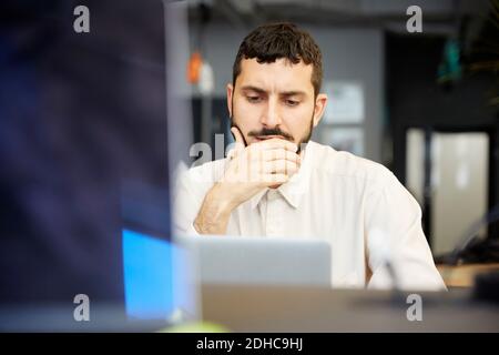 Homme d'affaires créatif stressé regardant un ordinateur portable tout en étant assis au bureau Banque D'Images