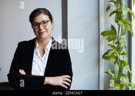 Portrait d'une femme d'affaires mûre souriante penchée sur un mur au bureau Banque D'Images