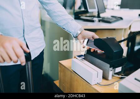 Section intermédiaire de l'homme d'affaires qui scanne le billet sur un smartphone à l'aéroport comptoir d'enregistrement Banque D'Images