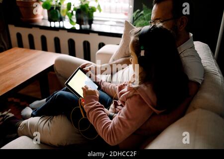 Vue en grand angle de la fille à l'aide d'une tablette numérique lorsque vous êtes assis avec le père sur le canapé à la maison Banque D'Images
