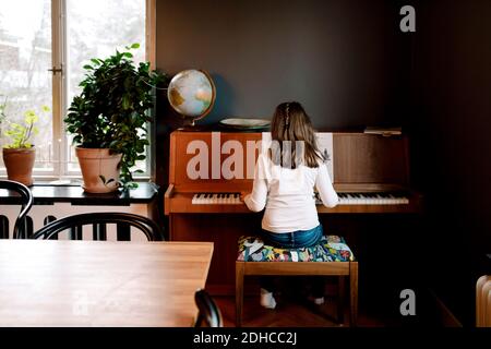 Vue arrière d'une fille jouant au piano tout en étant assise dans la vie chambre à la maison Banque D'Images