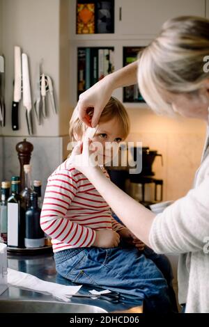 Mère appliquant le bandage sur le visage de la fille dans la cuisine à la maison Banque D'Images