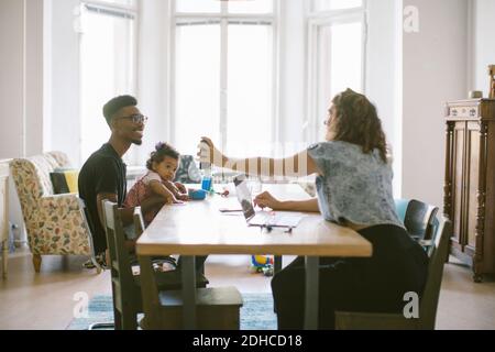 Femme montrant un téléphone portable à un homme assis avec sa fille à table dans la maison Banque D'Images