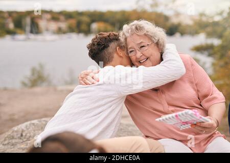 Petit-fils embrassant la grand-mère souriante tout en recevant un cadeau sur le bord du lac garez-vous pendant le pique-nique Banque D'Images